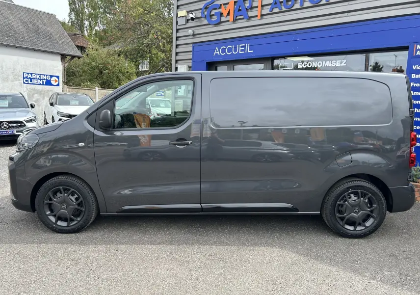 Profil côté gauche d'un utilitaire Citroën Jumpy gris titane 2025 avec jantes noires devant un garage automobile.