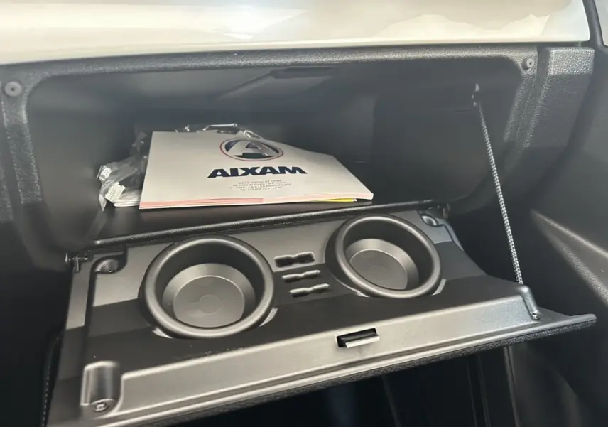 Intérieur de l’AIXAM AMBITION 0.5 CROSSOVER PREMIUM 2026, boîte à gants ouverte avec porte-gobelets intégrés.