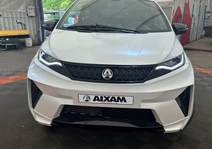Vue de face de l'AIXAM AMBITION 0.5 CROSSOVER PREMIUM blanc avec calandre noire et rétroviseur caméra côté gauche.