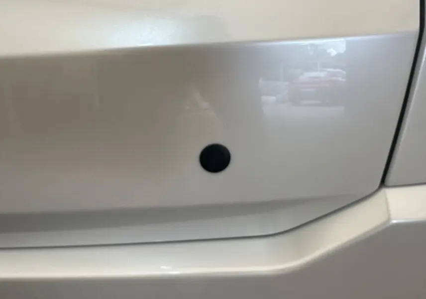 Gros plan sur la carrosserie blanche de l'AIXAM AMBITION 0.5 CROSSOVER PREMIUM, montrant un capteur noir intégré.