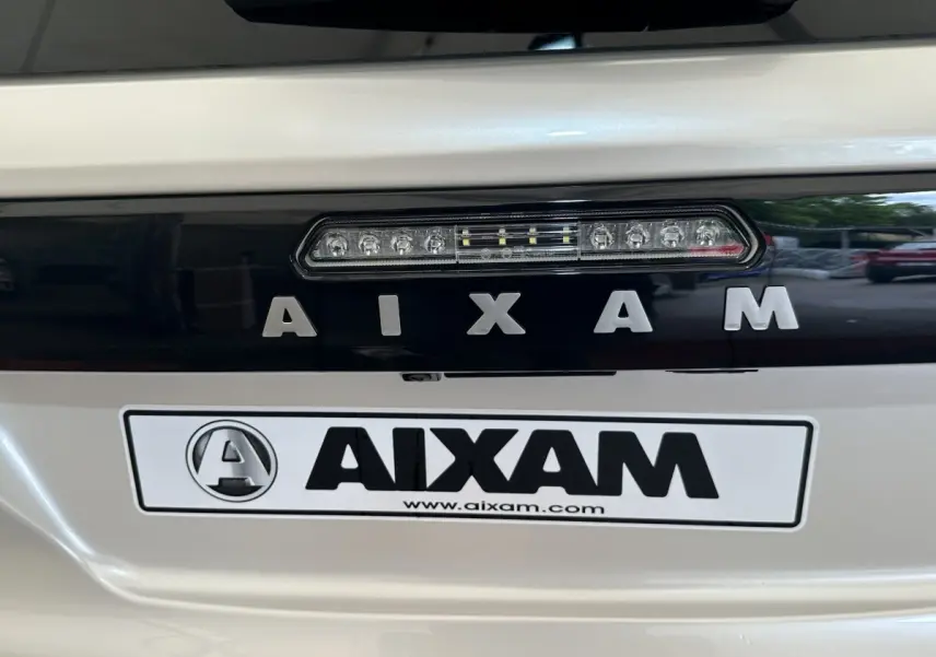 Gros plan arrière sur le logo AIXAM en lettres argentées sur fond noir, carrosserie blanche brillante.