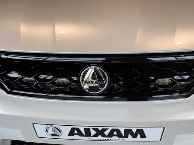 Gros plan sur la calandre noire et le logo Aixam d’un véhicule blanc, vue frontale centrée.