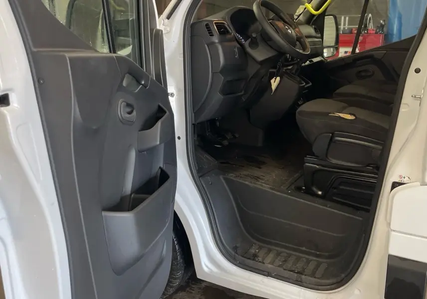 Vue intérieure côté conducteur du Renault Master blanc 2020, montrant l'ouverture de porte et les sièges noirs.