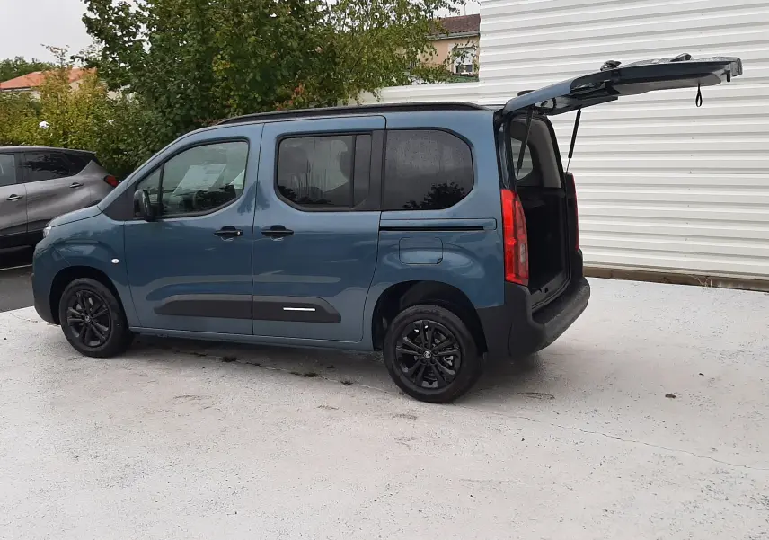 Vue 3/4 arrière droite du Citroën Berlingo bleu Kiama avec hayon ouvert et jantes noires sur parking extérieur.