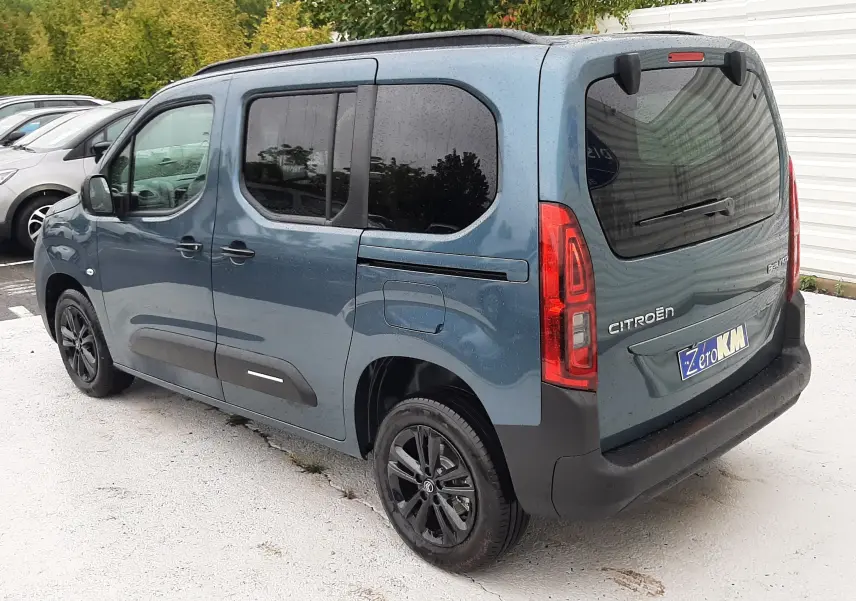 Vue 3/4 arrière droite d'un Citroën Berlingo bleu Kiama avec vitres teintées et jantes noires, stationné en extérieur.