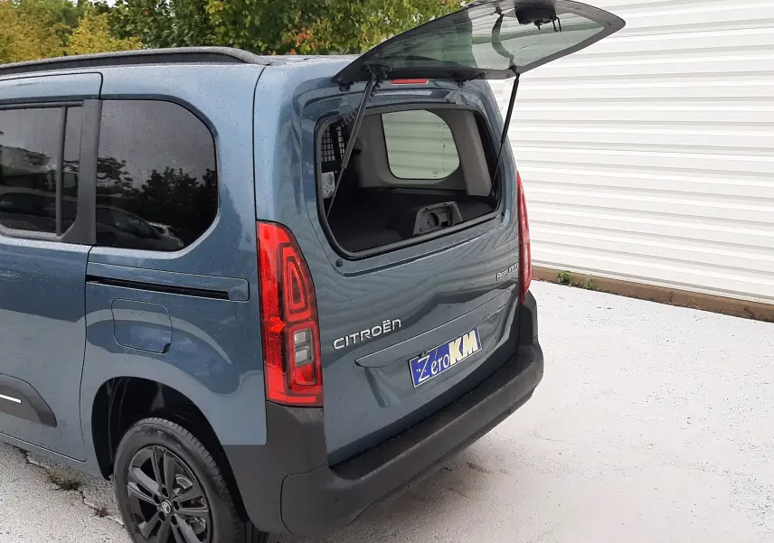 Vue 3/4 arrière droite d'un Citroën Berlingo bleu Kiama 2026 avec hayon arrière ouvert et feux arrière allumés.