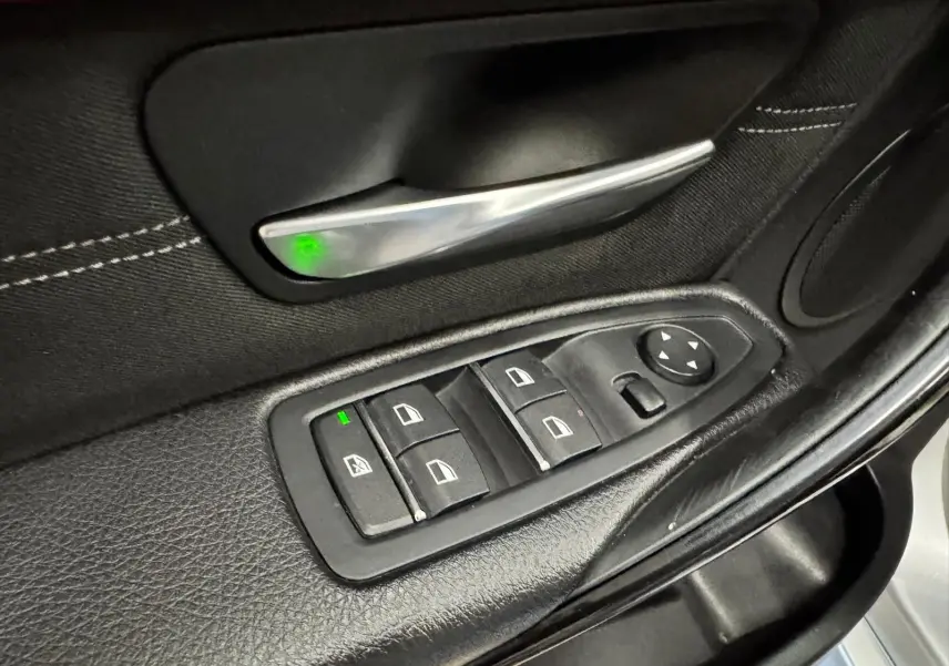 Détail de la commande des vitres électriques sur la portière noire côté conducteur d'une BMW Série 3 Touring gris aluminium.