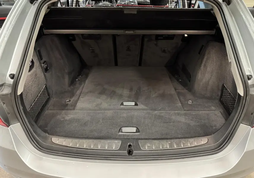 Vue arrière du coffre spacieux et vide d'une BMW Série 3 Touring F31 gris aluminium, avec tapis noir et filet latéral.