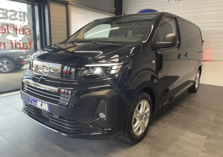 Opel Vivaro noir carbone en showroom, vue 3/4 avant droit avec phares allumés et jantes argentées.