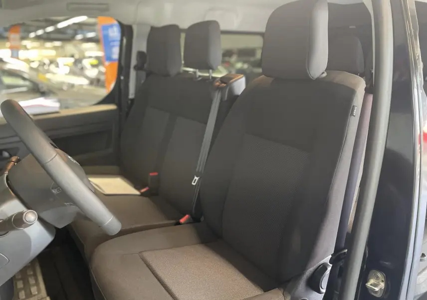 Vue intérieure côté conducteur du double cabine Opel Vivaro 2025 noir carbone, sièges tissu bi-ton noir/gris avec appuie-têtes.