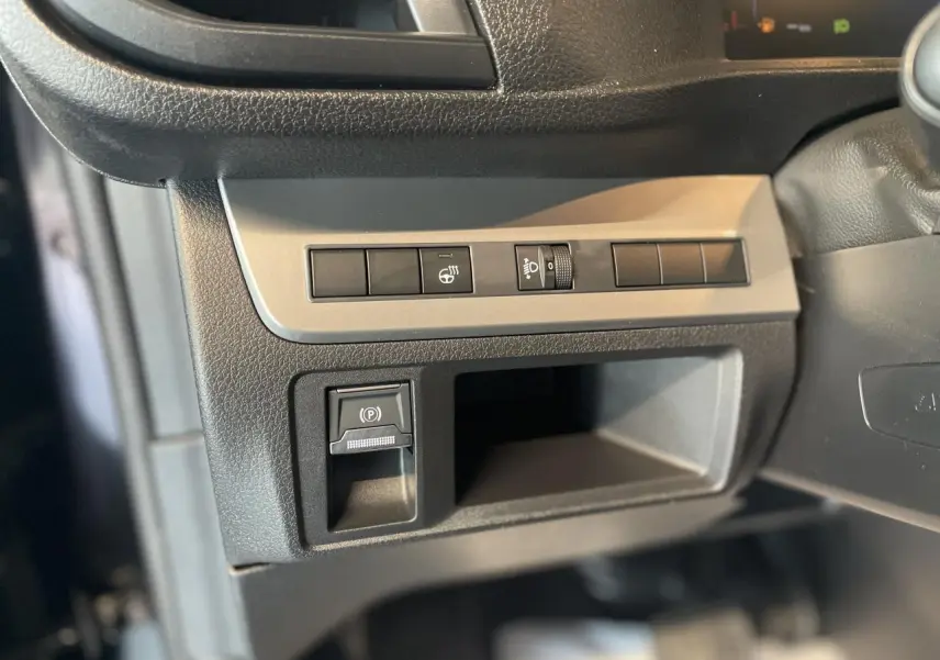 Gros plan sur les commandes de réglage des phares et frein à main électrique dans l'habitacle noir du Opel Vivaro 2025.