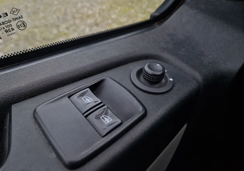 Gros plan sur les commandes des vitres électriques et réglage des rétroviseurs côté gauche du Renault Trafic Fourgon blanc L1H1 2019.