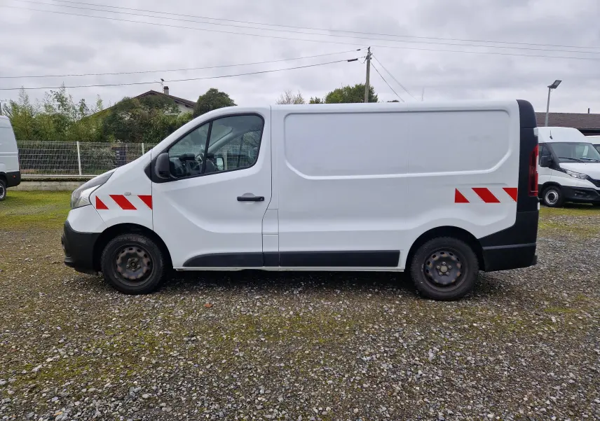 Vue de profil côté gauche d’un Renault Trafic Fourgon blanc avec bandes réfléchissantes rouges sur l’aile avant et l’arrière.