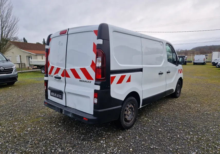 Renault Trafic Fourgon blanc vu en 3/4 arrière droit avec bandes rouges réfléchissantes sur portes et flanc.