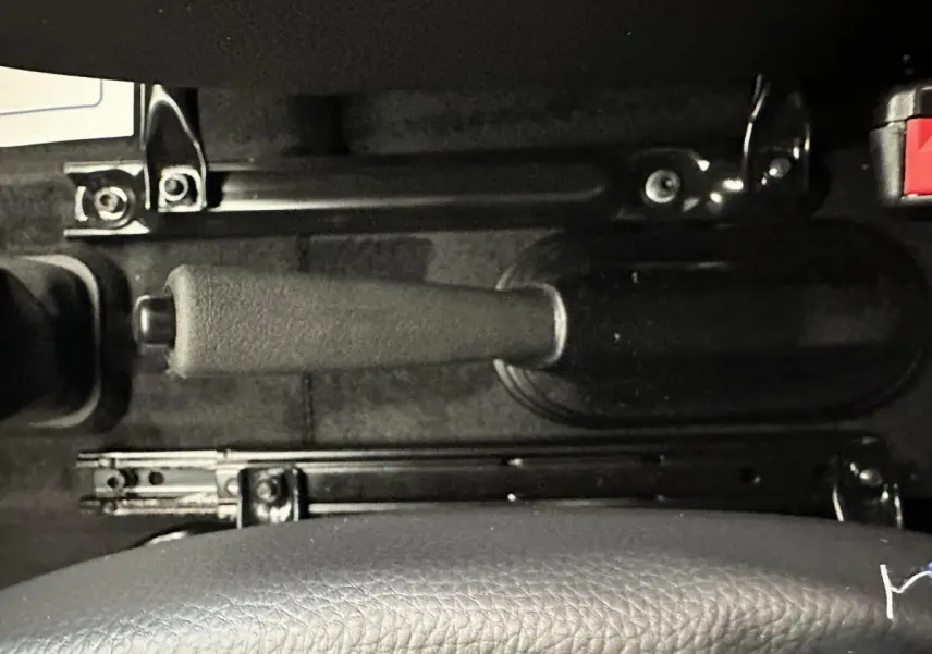 Gros plan sur le frein à main noir et la partie inférieure du siège en cuir dans l'habitacle de l'AIXAM Ambition bleu.