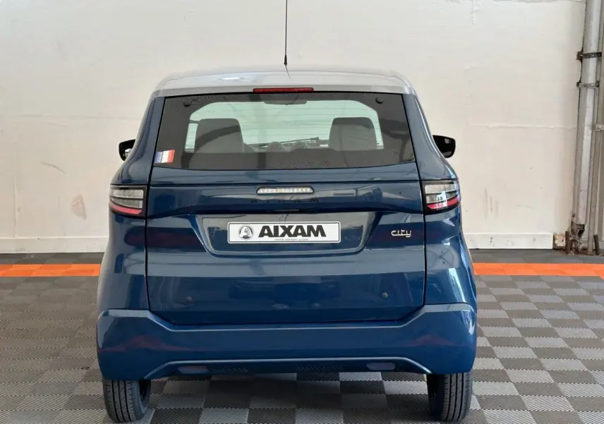 Vue arrière d'une AIXAM Ambition 0.5 City Pack bleu 2026 avec plaque et vitres teintées, stationnée en intérieur.