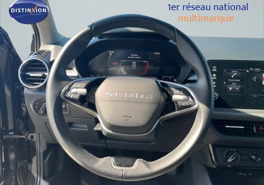 Vue intérieure centrée sur le volant SKODA d'une Fabia 2025 noire, avec tableau de bord numérique et écran tactile visible.