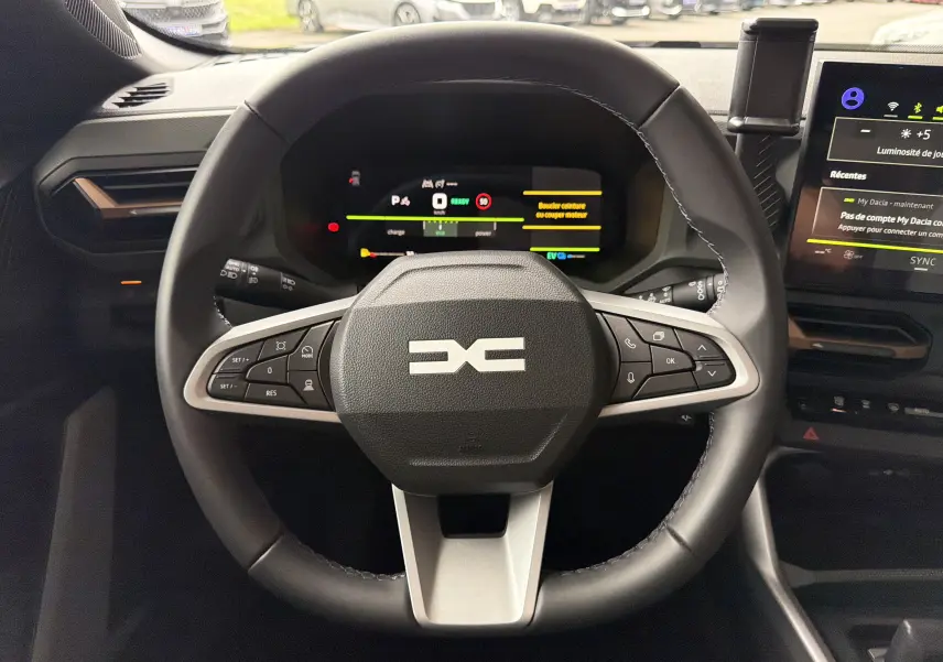 Vue intérieure centrée sur le volant multifonction du Dacia Bigster Hybrid 155, avec tableau de bord numérique et écran tactile.
