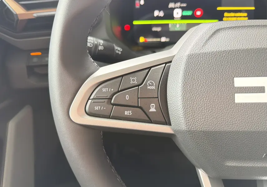 Gros plan sur les commandes à gauche du volant du Dacia Bigster Hybrid 155, intérieur noir avec affichage numérique flou.