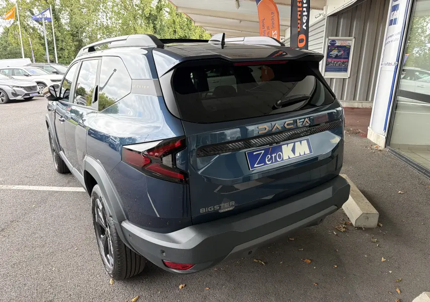 Vue 3/4 arrière droite du Dacia Bigster Hybrid 155 Extreme bleu indigo avec barres de toit et jantes diamantées.