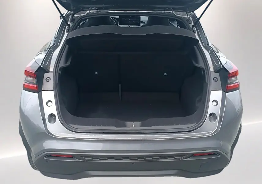 Vue arrière du coffre ouvert d'un Nissan Juke gris 2025, montrant l'espace de chargement vide et les feux arrière LED.