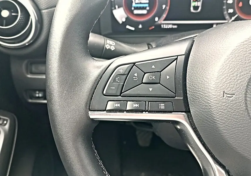 Gros plan sur le volant cuir noir multifonction du Nissan Juke gris, avec commandes audio et écran numérique en arrière-plan.
