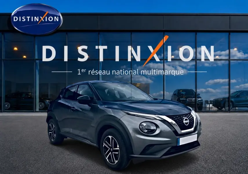Nissan Juke gris en 3/4 avant droit, avec calandre V-Motion chromée et jantes alliage noires.