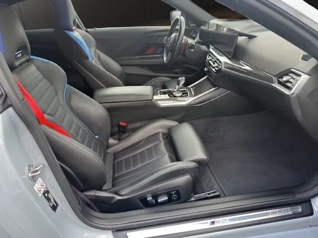 Intérieur côté conducteur d'une BMW M2 G87 gris Brooklyn avec sièges sport noirs et surpiqûres rouges et bleues.