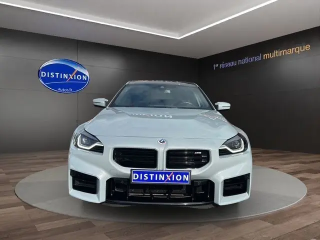 Vue frontale d'une BMW M2 G87 gris Brooklyn Grau avec calandre noire et phares LED dans un showroom.