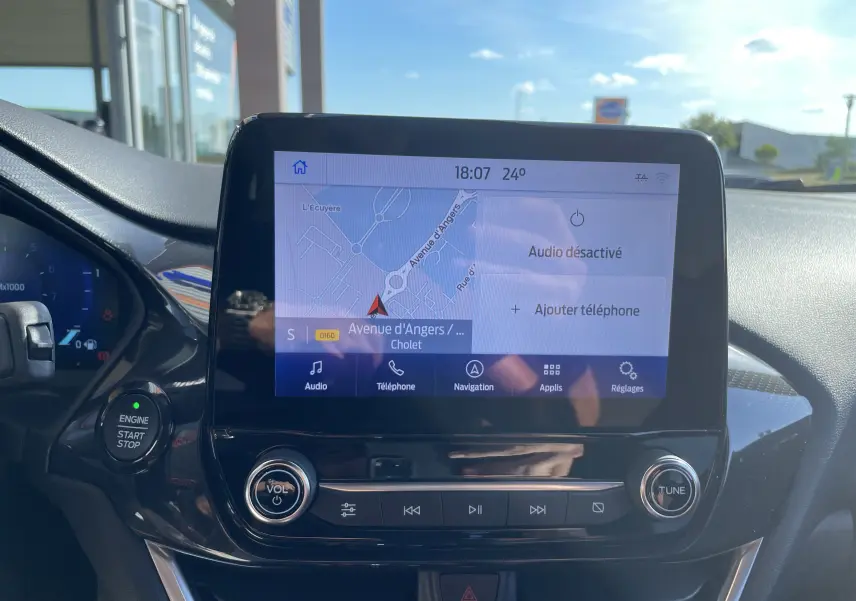 Vue rapprochée de l'écran tactile central du Ford Puma 1.0I 125 MHEV rouge, affichant la navigation et commandes audio.