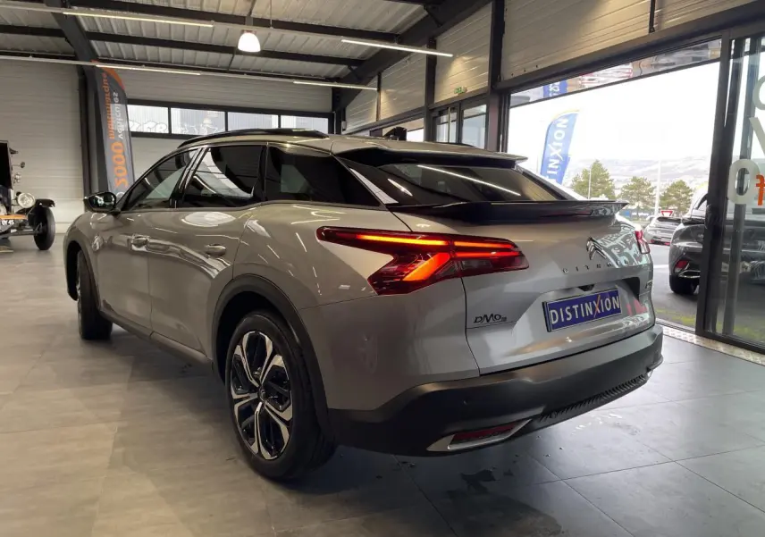 Vue 3/4 arrière droite d'une Citroën C5 X 2024 gris foncé avec feux arrière allumés dans un showroom.