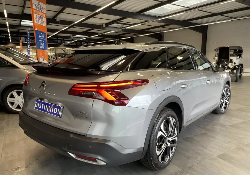 Vue 3/4 arrière droite d'une Citroën C5 X 2024 gris foncé avec feux arrière allumés en concession.