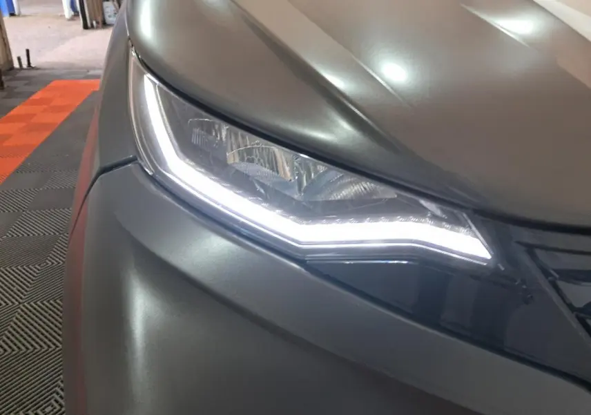 Gros plan sur le phare avant droit gris clair de l’Aixam Ambition 2024 avec éclairage LED distinctif allumé.