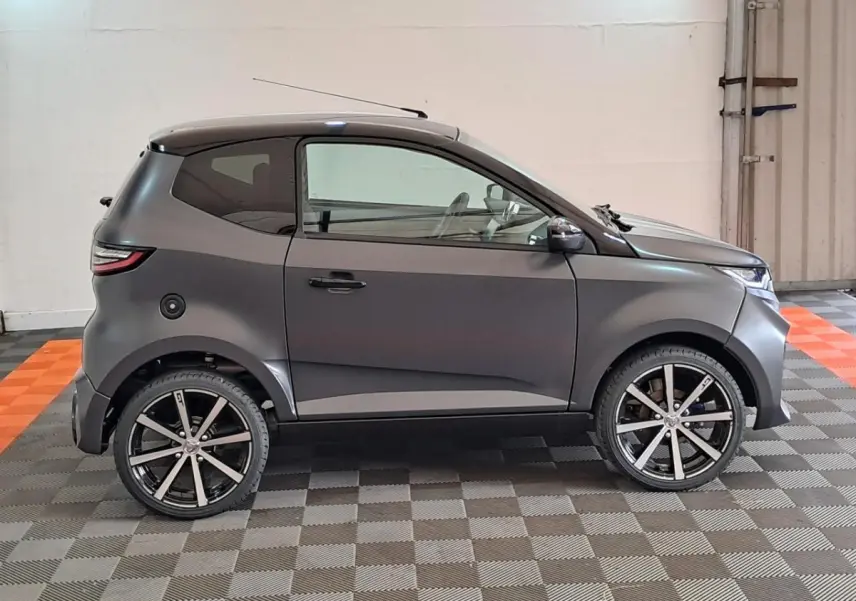 Vue de profil droit d'une Aixam Ambition 2024 gris clair avec jantes alliage noires diamantées et rétroviseurs chromés.