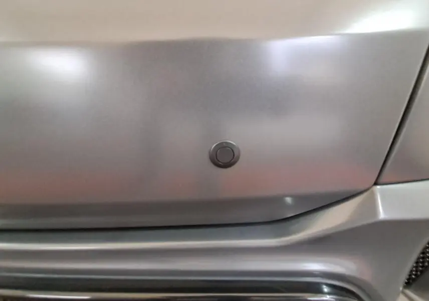 Gros plan sur le pare-chocs gris clair de l'Aixam Ambition 2024, mettant en valeur un capteur de radar de recul intégré.