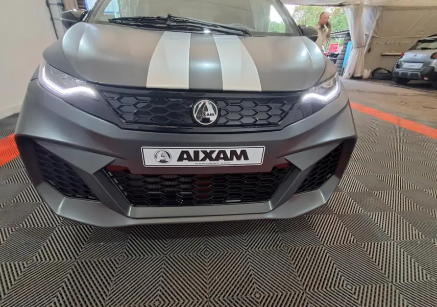 Vue frontale rapprochée de l'AIXAM AMBITION gris clair avec bandes blanches et éclairage LED distinctif.