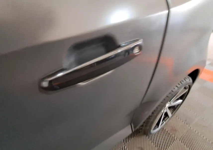 Gros plan sur la poignée de porte côté gauche d’une Aixam Ambition gris clair avec jante alliage noire diamantée visible.