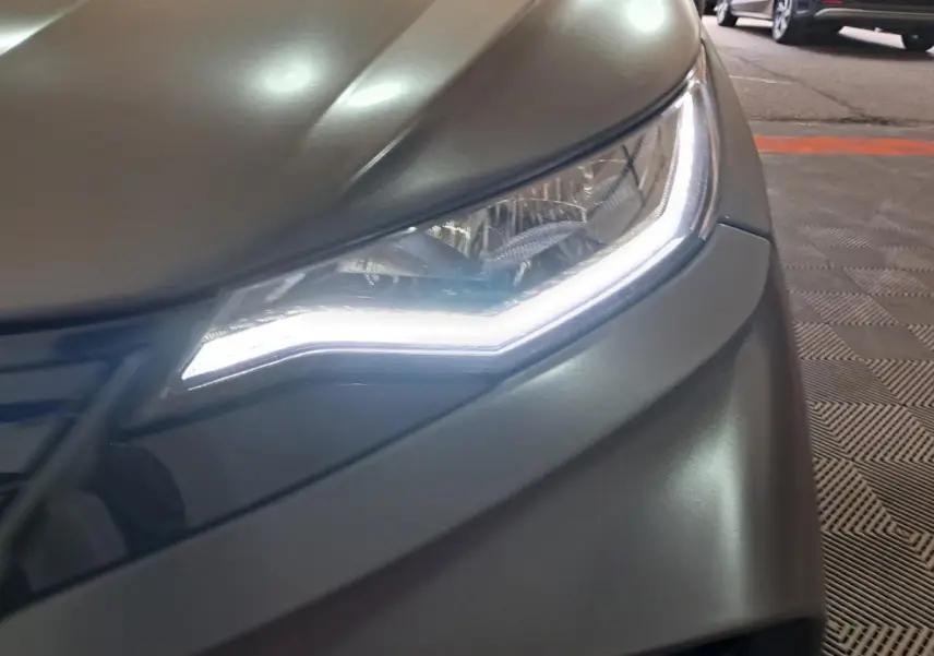 Gros plan sur le phare avant droit d'une Aixam Ambition 2024 gris clair avec éclairage LED distinctif.