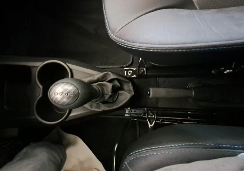 Vue plongeante sur la console centrale de l'AIXAM AMBITION 2024, avec levier de vitesse et frein à main entre sièges gris clair.