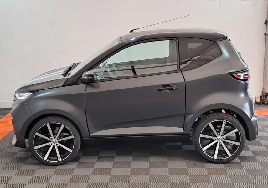 Vue de profil côté gauche de l'Aixam Ambition 2024 gris clair avec jantes alliage noires diamantées et lignes épurées.