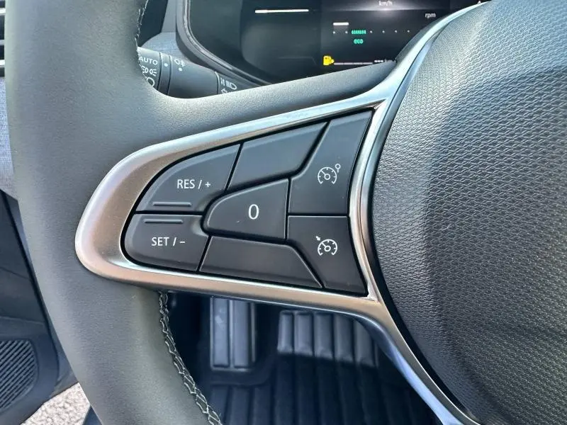 Gros plan sur les commandes du régulateur de vitesse à gauche du volant de la Renault Clio gris Rafale 2025.