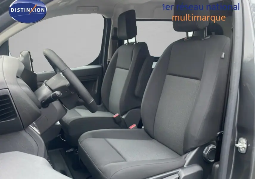 Vue intérieure côté conducteur du Citroën Jumpy Long L3 gris titane, montrant les sièges avant en tissu noir et gris.
