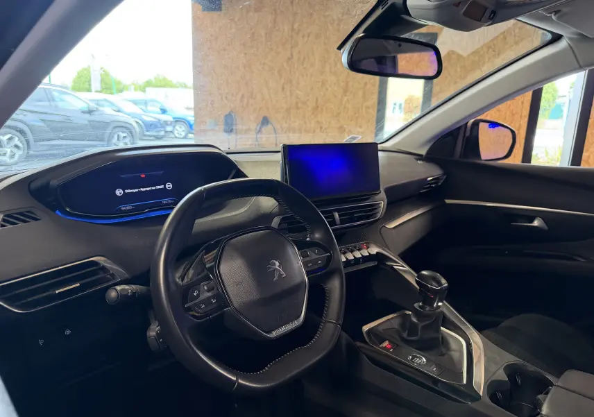 Vue intérieure côté conducteur du Peugeot 5008 gris 2021, mettant en valeur le volant compact, l'écran central et la boîte manuelle.