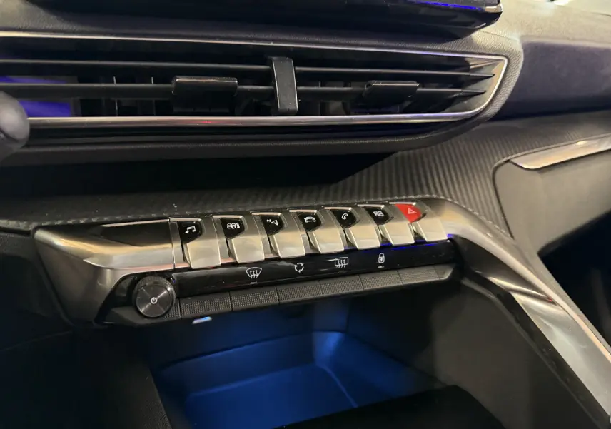 Vue rapprochée de la console centrale du Peugeot 5008 gris, mettant en valeur les commandes piano et l’éclairage d’ambiance bleu.