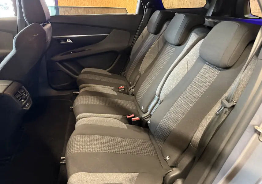 Vue latérale droite de l'intérieur arrière du Peugeot 5008 gris 2021, montrant les sièges en tissu noir et gris à motifs.