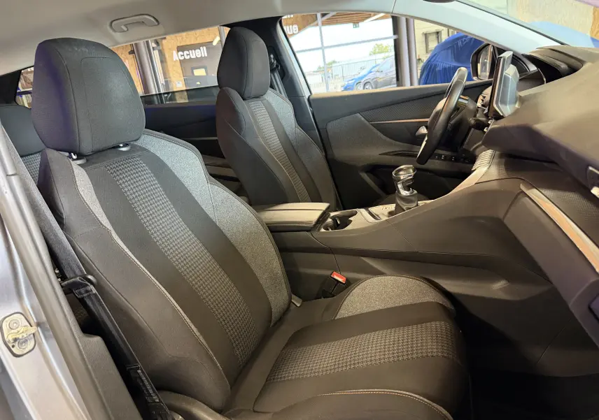 Vue intérieure côté conducteur du Peugeot 5008 gris 2021, mettant en valeur les sièges tissu noirs et la console centrale avec boîte manuelle.