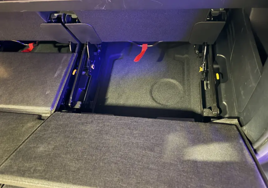 Vue rapprochée de la zone de rangement sous les sièges arrière du Peugeot 5008 gris, montrant les fixations et sangles rouges.