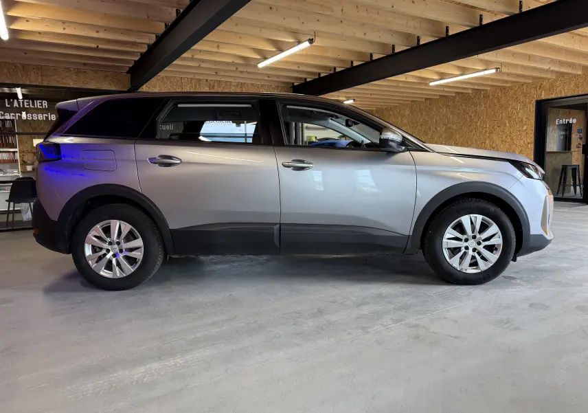 Vue latérale droite d’un Peugeot 5008 gris 2021 dans un garage avec intérieur en bois et éclairage fluorescent.