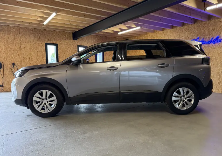 Peugeot 5008 gris vue de profil côté gauche, SUV 5 portes avec jantes alliage et toit noir dans un garage.