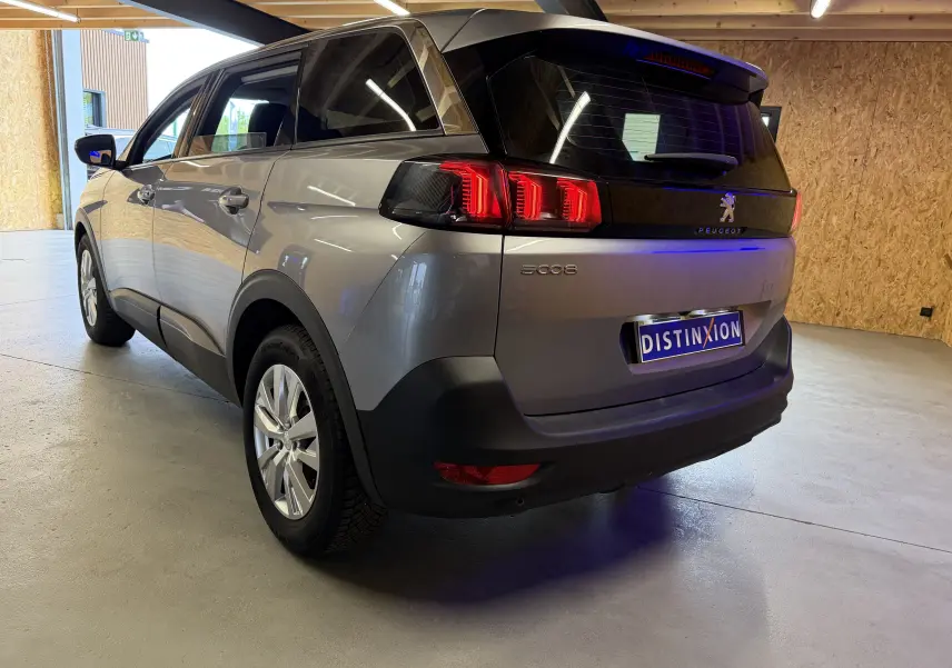 Peugeot 5008 gris vue 3/4 arrière droit, feux arrière allumés dans un garage en bois.